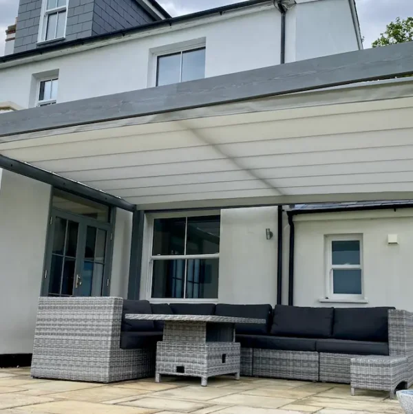 How much does a pergola cost to buy? Image of a pergola with retractable shade against a house.